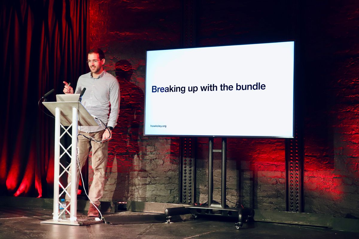 Joel standing on a stage next to a TV on a stand with a presentation slide that says "Breaking up with the bundle"