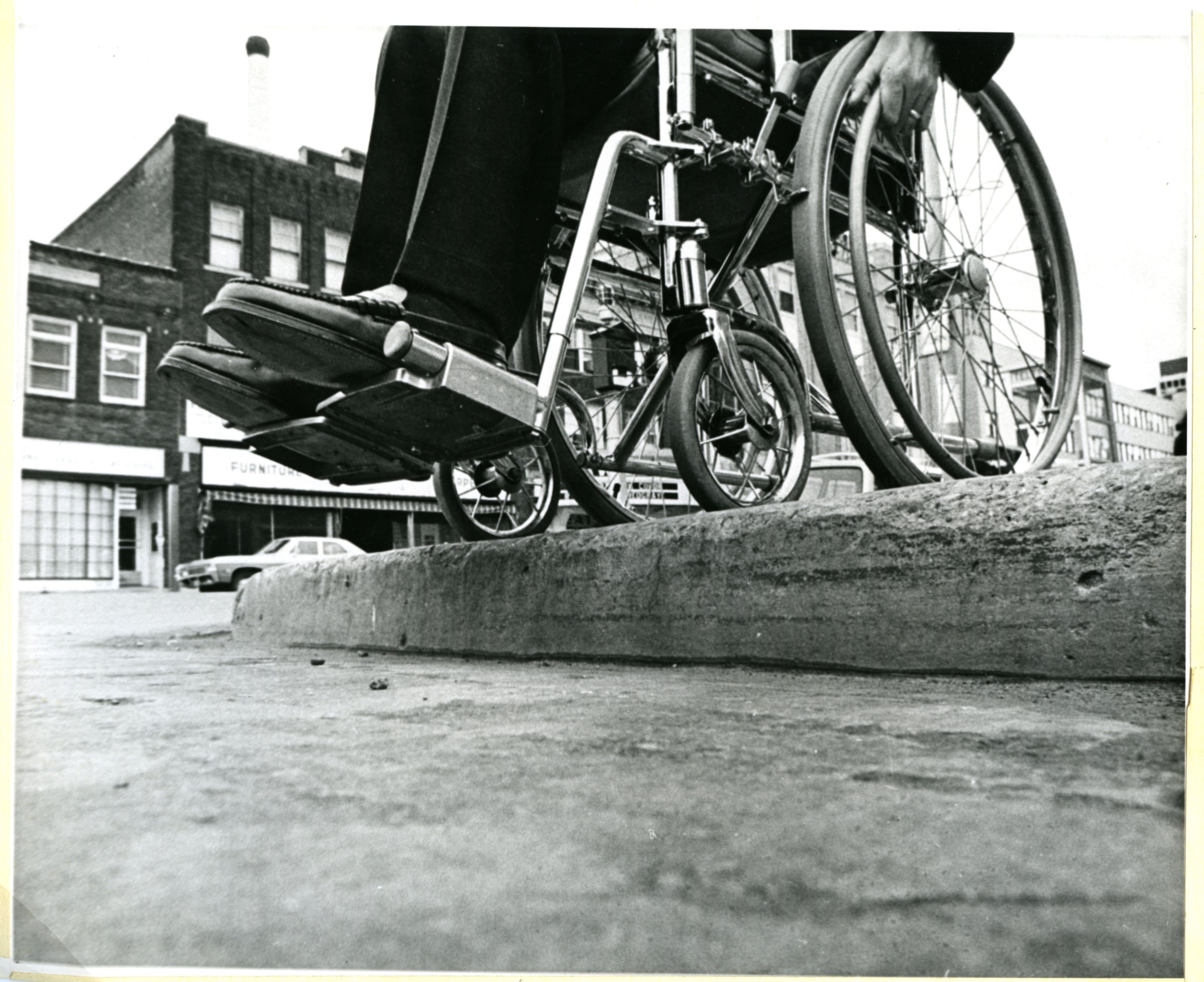 Picture of a wheelchair user above an uncut curb, shot from street level