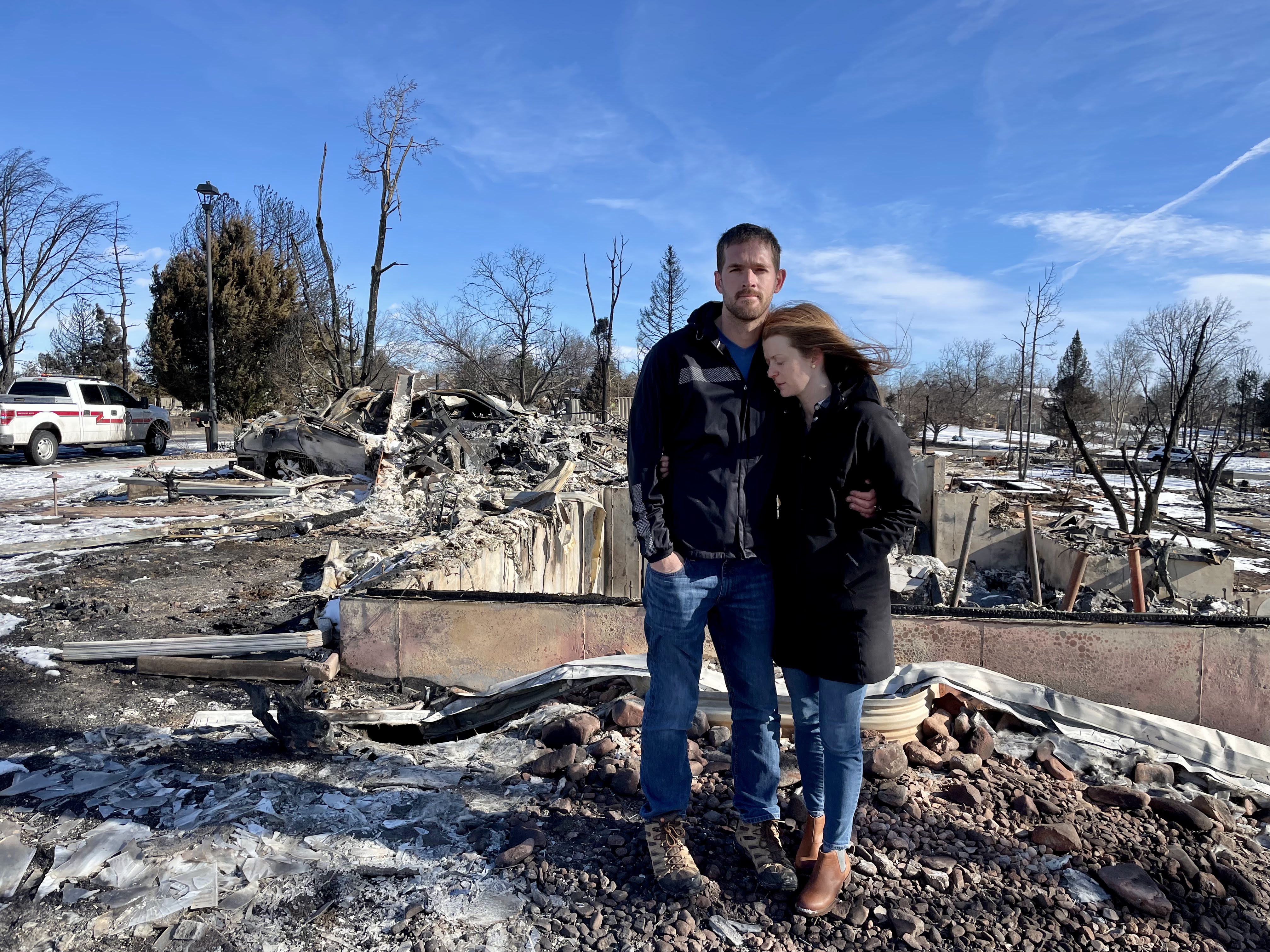 A couple stands in front of a burned down house