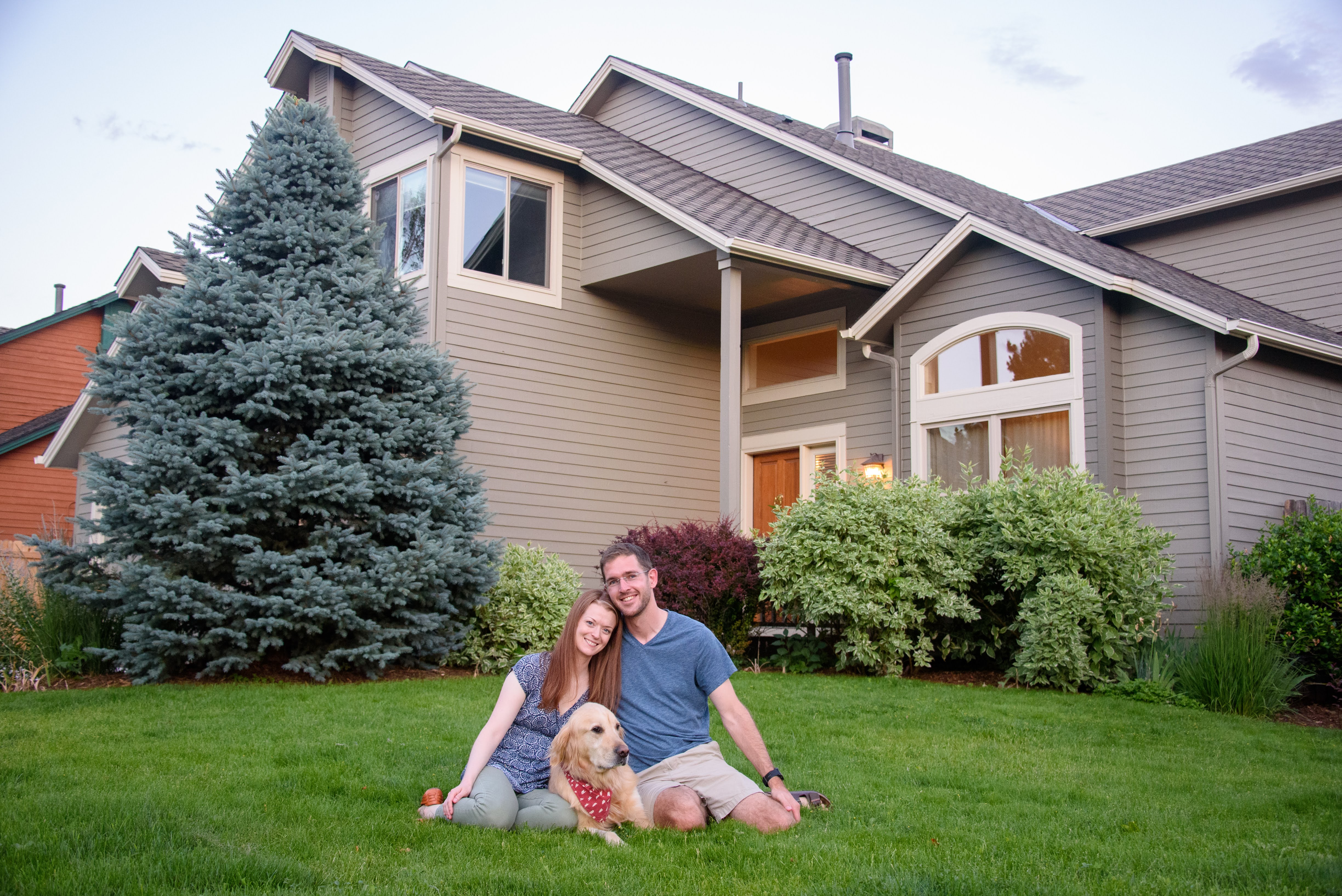 Family sits with their dog in the lawn in front of their home