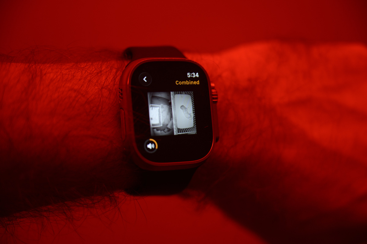 A feed of two baby monitors is displayed on an Apple Watch. There is dramatic red lighting in the room.