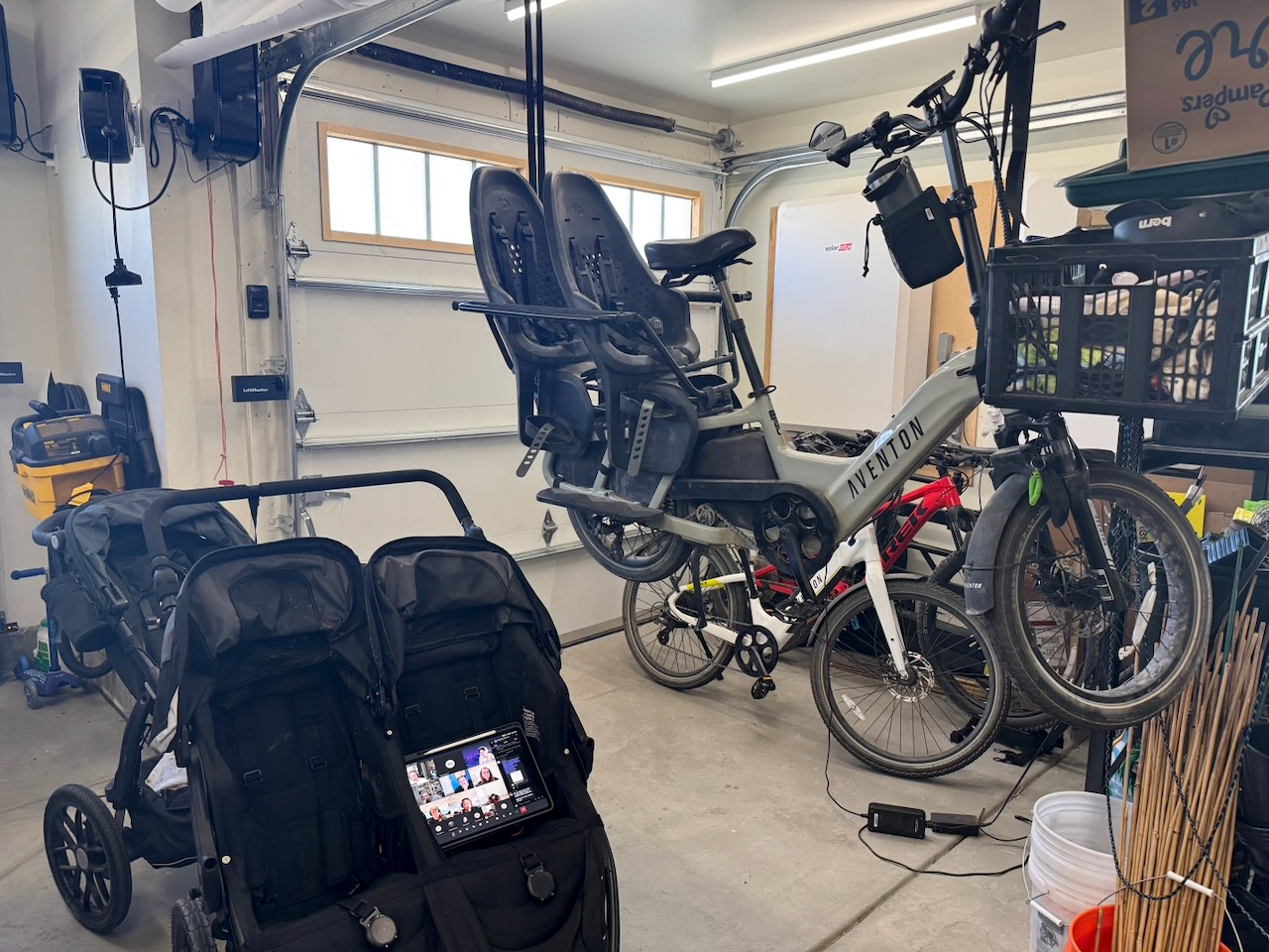 An iPad sits in a stroller displaying a video call while a bike hangs in the air on a pulley.