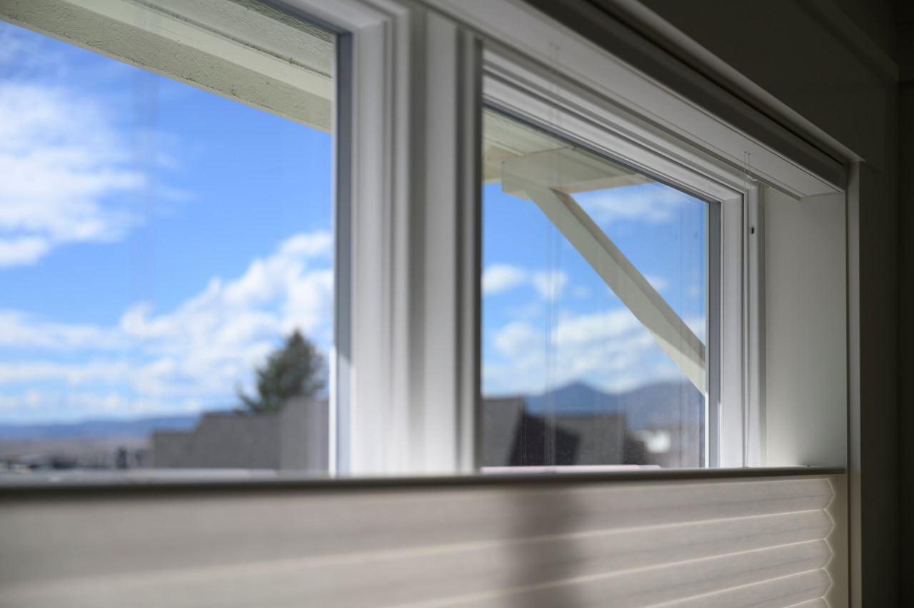 A top-down shade partially covers a window, leaving a view of blue sky and mountains above it.