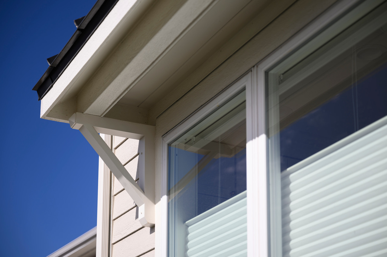 An exterior view of a window with a partially lowered top-down shade and a roof overhang casting a shadow above it.