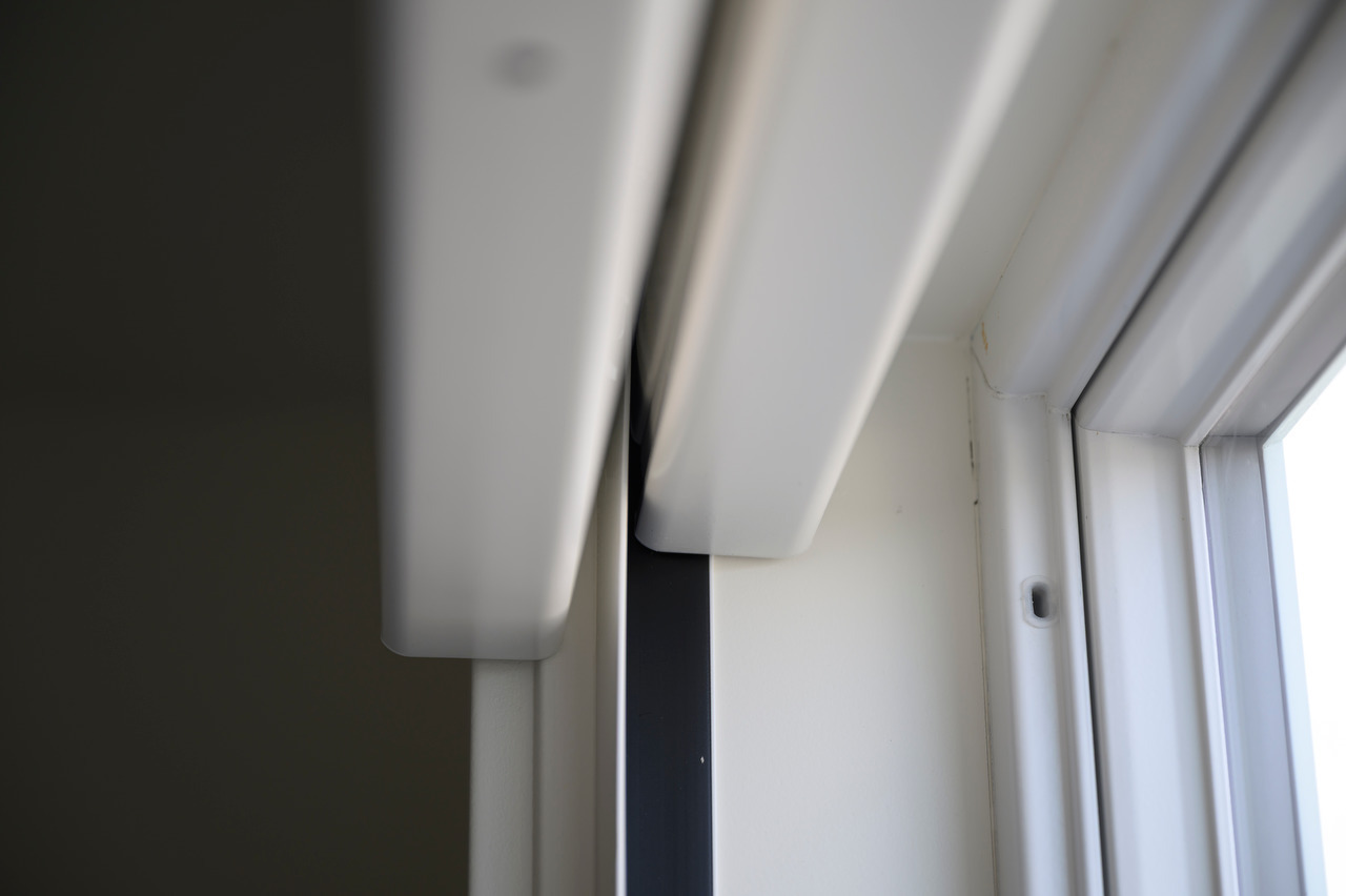 A close-up of two shade headrails with a light-blocking channel between them, painted to match the white window trim.